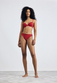 Red lace bra and matching thong, featuring scalloped edges and a small logo detail. Soft texture, sleek design, and vibrant color.