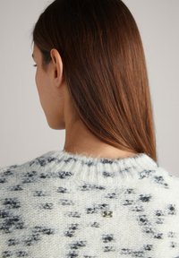 Maglione cream con un motivo testurizzato in grigio scuro, caratterizzato da un colletto a costine e un piccolo logo metallico vicino al collo sul retro.