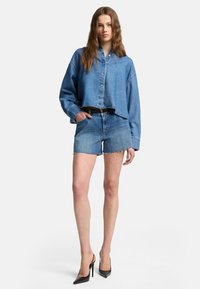 Jeansjacka med kort längd i blå nyanser, knäppning fram, och avslappnad passform, matchad med jeansshorts och svarta högklackade skor.