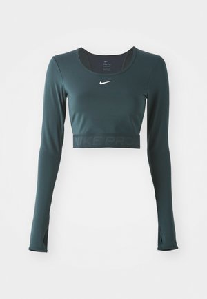 Långärmad crop top i mörkgrön, tillverkad av mjukt tyg. Har Nike-logotyp i vitt, tumhål och texturerad band med "NIKE PRO"-bokstäver.