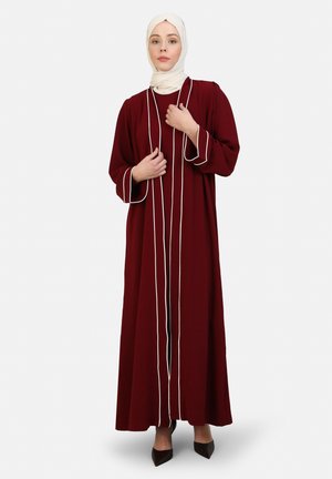 Abaya color melanzana con maniche lunghe, caratterizzata da accenti di piping bianco. Il tessuto appare morbido e fluido, raggiunge le caviglie, abbinata a un hijab beige.