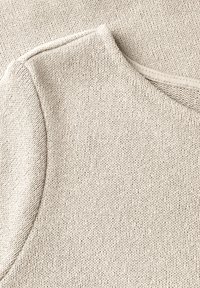 Beige stickad topp med rund halsringning och korta ärmar, med en mjuk struktur och ett subtilt ribbat mönster längs kanterna.