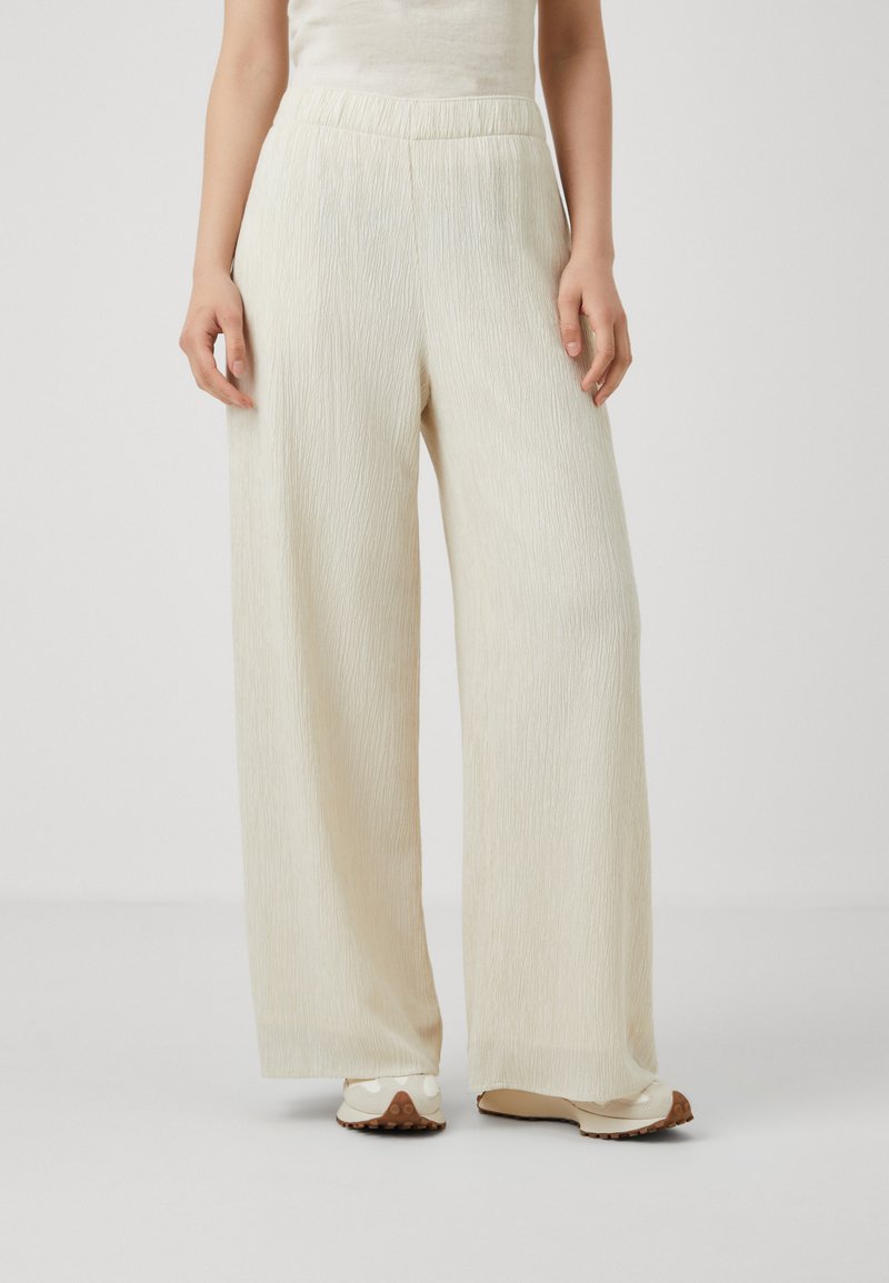 Pantalons larges de couleur crème clair, dotés d'un tissu texturé avec de fines rayures verticales et d'une taille élastique.