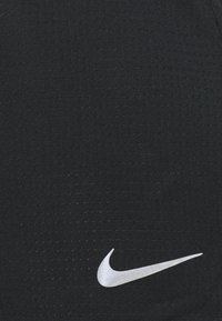 Pantalones cortos deportivos negros hechos de una tela texturizada, con un prominente logo blanco de Nike en la parte inferior frontal. Diseño simple y forma ajustada.
