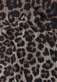 Tkanina s leopardím vzorem v béžové a černé barvě, s texturovaným, plisovaným designem. Materiál má jemný, lehký vzhled.