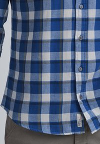 Blå og hvit rutete skjorte med plaidmønster. Har knapper og buet søm. Laget av et strukturert stoff med en avslappet passform.