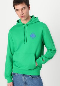 Felpa verde realizzata in tessuto morbido, con tasca frontale, cappuccio con coulisse e logo ricamato viola con motivo tennistico.
