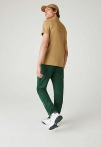 Tan pikétröja, gröna sportbyxor med dragkedjor vid anklarna, och vita sneakers. Stilen är avslappnad och sportig.