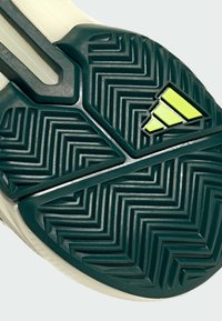 Semelle en caoutchouc épais avec un motif en zigzag ; vert foncé avec une touche de jaune. Présente un design texturé pour une meilleure traction et stabilité.