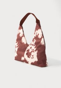 Saco de ombro com padrão de pele de vaca castanha e branca, com alça larga, tecido suave e formato triangular.