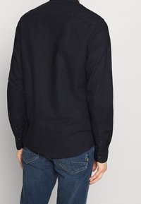 Zwarte blouse met lange mouwen, gemaakt van katoen, met een kraag, rechte snit en subtiele textuur. Gedragen met blauwe spijkerbroek.