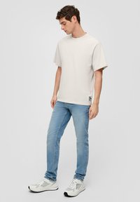 Jasnoszary bawełniany t-shirt z krótkim rękawem, w zestawieniu z jasnoniebieskimi dżinsami i białymi butami sportowymi z szarymi akcentami. Prosty wzór, luźny krój.