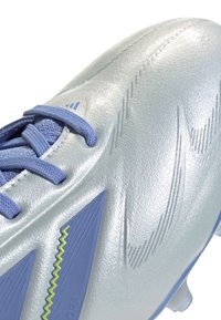 Sølv fotballsko med teksturert syntetisk materiale, lyseblå snøring og skrå blå detaljer. Har strømlinjeformet design og teksturert overflate.