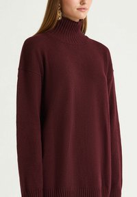 Maglione borgogna con collo alto a coste, vestibilità ampia, spalle scese e motivo lavorato a maglia texturizzato. Presenta polsini e orlo a coste.