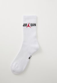 Calcetín deportivo blanco con textura acanalada. Presenta "JORDAN" en letras negras y un logotipo Jumpman rojo. Punta redondeada y talón reforzado.