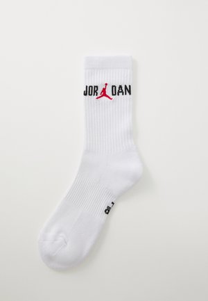Hvid sportssok med ribbet tekstur. Har "JORDAN" i sort skrifttype og et rødt Jumpman-logo. Rund tå og forstærket hæl.