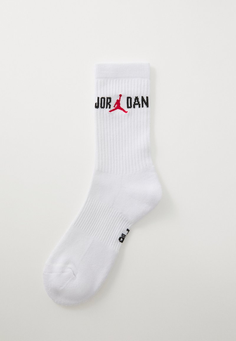 Calcetín deportivo blanco con textura acanalada. Presenta "JORDAN" en letras negras y un logotipo Jumpman rojo. Punta redondeada y talón reforzado.