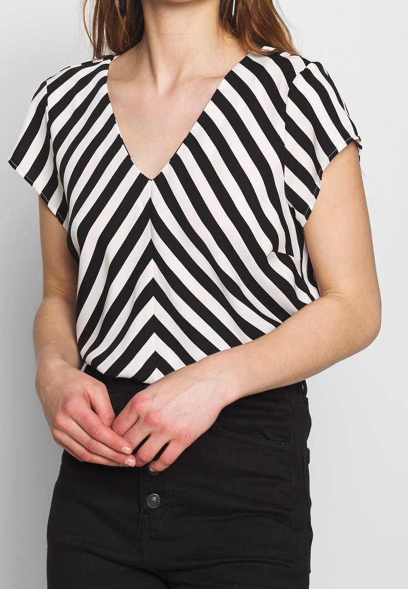 Sort og hvid-striped bluse med v-udskæring, korte ærmer og en løs pasform. Striberne veksler mellem brede og smalle mønstre.