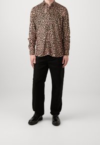 Leopardprint overhemd met knoopsluiting in roze en zwart, gecombineerd met zwarte broek en zwarte schoenen. Het shirt heeft lange mouwen en een kraag.