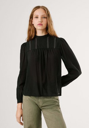 Zwarte blouse met lange mouwen en hoge hals, met geplooide pofmouwen en witte stiksels op de borst. Zachte, gestructureerde stof.