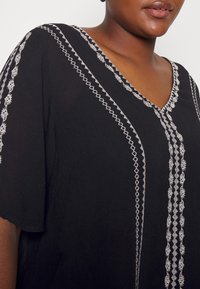 Svart tunika med silverbroderi längs V-ringningen och ärmarna, med en lös, flödande design och texturerad tyg.