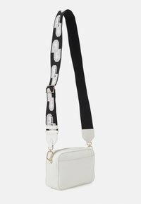 Biała skórzana torba na ramię o prostokątnym kształcie, z zamkiem błyskawicznym i odpinanym czarnym paskiem z białymi akcentami logo.