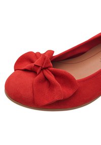 Zapato plano de ante rojo con un gran lazo en la puntera, forma redonda y un forro interior suave, con una suela exterior ligeramente texturizada.
