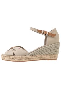Sandali con zeppa beige, design frontale annodato, cinturino alla caviglia regolabile e dettagli in juta intrecciata sul tallone per un'aggiunta di texture e contrasto.