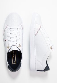 Białe sneakersy na sznurowadła z teksturowaną cholewką, okrągłym noskiem, złotymi oczkami i czarnym akcentem na pięcie. Gładki, minimalistyczny design z subtelnym logo.