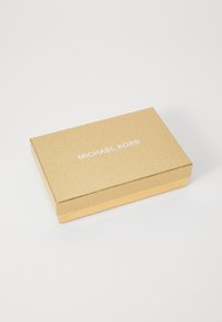 Zlatna kutija za poklone s teksturiranom površinom, s bijelim brendom "MICHAEL KORS", pravokutnog oblika i sjajnom zlatnom bazom u kontrastu.