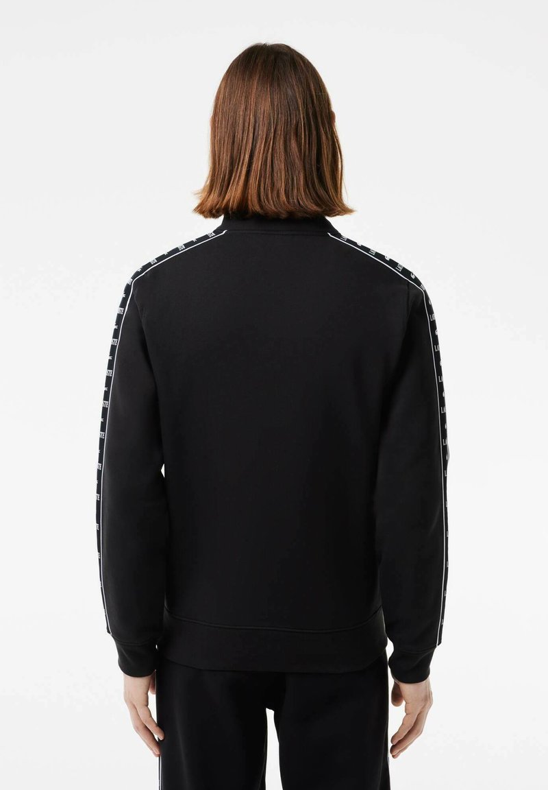 Schwarzer Kapuzenpullover mit hohem Kragen, ausgestattet mit weißen Seitenstreifen und bedrucktem Logo-Detail. Lange Ärmel mit gerippten Bündchen. Einfaches Design.