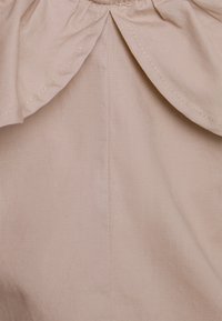 Primer plano de una tela beige con costuras detalladas y una costura fruncida que crea un ligero volante en la parte superior central.