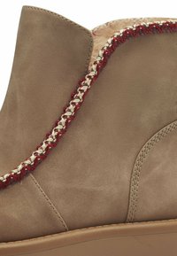 Tanen leren enkelboot met een gevlochten rode en crèmekleurige textielaccent langs de kraag, met lichte stiksels en een rubberen zool.