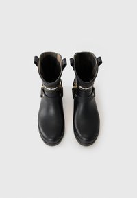 Ζευγάρι μαύρων ankle μποτών Barbour με καρό εσωτερική επένδυση, χρυσές αγκράφες και λαβές, με θέα από πάνω σε ανοιχτό φόντο.