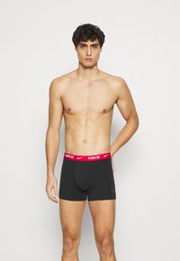 Calzoncillos de algodón negro con una cinturilla elástica roja que presenta el logotipo "NIKE" y un pequeño logotipo en la pierna, ajuste ceñido, longitud a mitad del muslo.