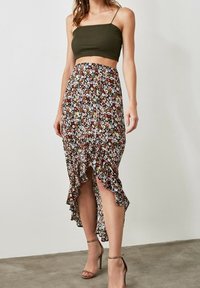Rok midi bunga dengan hem tinggi-rendah dan aksen ruffle, menampilkan dasar gelap dengan pola bunga berwarna-warni. Dipadukan dengan crop top hijau yang pas.