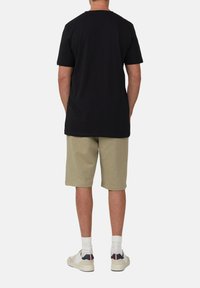 Zwarte katoenen T-shirt en beige shorts. Het T-shirt heeft een relaxte pasvorm; de shorts zijn boven de knie met een elastische tailleband. Witte sneakers met accenten.