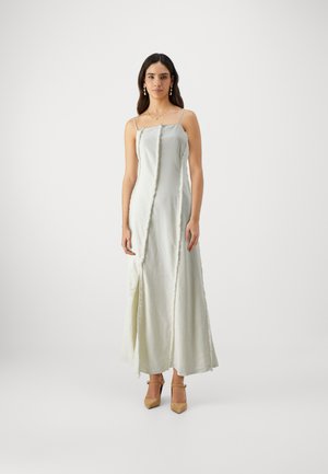 Lång, ljusgrön satin-klänning med tunna band, som har en central slits och texturerade vertikala sömdetaljer. Bärs med beige klackar.
