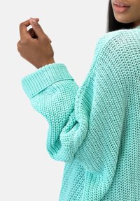 Helles mintgrünes Strickpullover mit einem lockeren, strukturierten Design, breiten Rippbündchen und einer offenen, lässigen Passform.
