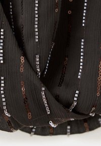 Black fabric with vertical lines of small white and brown sequins creating a textured, shiny striped pattern.