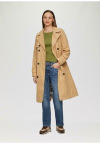 Beige trenchcoat met een losse pasvorm, dubbelgeknoopte knopen en een jasje met luipaardprint, gecombineerd met een groene top en blauwe jeans.