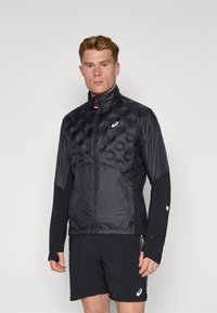 Schwarze Jacke mit einem gesteppten oberen Abschnitt, glattem unteren Abschnitt, hohem Kragen und Reißverschluss; mit rotem Reißverschlussanhänger und Logo.