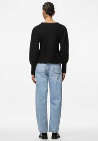 Czarny sweter dzianinowy z bufiastymi długimi rękawami i dopasowanym wcięciem w talii, zestawiony z jasnoniebieskimi dżinsami z wysokim stanem i czarnymi butami.
