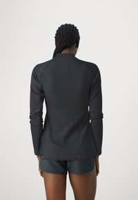 Black ribbed long-sleeve top with a fitted design, featuring a round neck and slightly extended sleeves, paired with dark shorts.