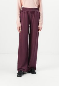 Wide-leg trousers in deep purple, made of a soft material. Features an elastic waistband and paired with black shoes.