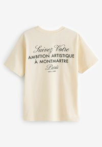 Tricou din bumbac de culoare crem, cu mâneci scurte, având un text negru: "Urmează-ți Ambiția Artistică la Montmartre Paris 1971-1980."
