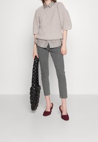 Pull en maille gris clair, chemise à rayures avec col, jean gris, chaussures slip-on tissées bordeaux et sac fourre-tout noir en tresse.