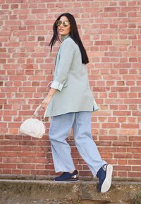 Lys blå oversized blazer, lys denim vide bukser, mørke sneakers med metalliske accenter, og beige håndtaske. Solbriller fullfører antrekket.