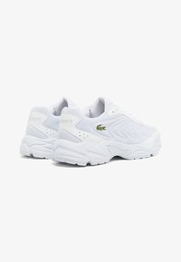 Baskets de sport blanches avec un dessus en mesh texturé, semelle en caoutchouc et accent du logo Lacoste en vert. Présente un bout arrondi et un collier rembourré.