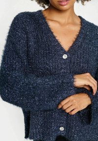Dark blue, fluffy cardigan with a V-neck, long sleeves, and silver button closure. Soft texture with a subtle shimmer throughout.